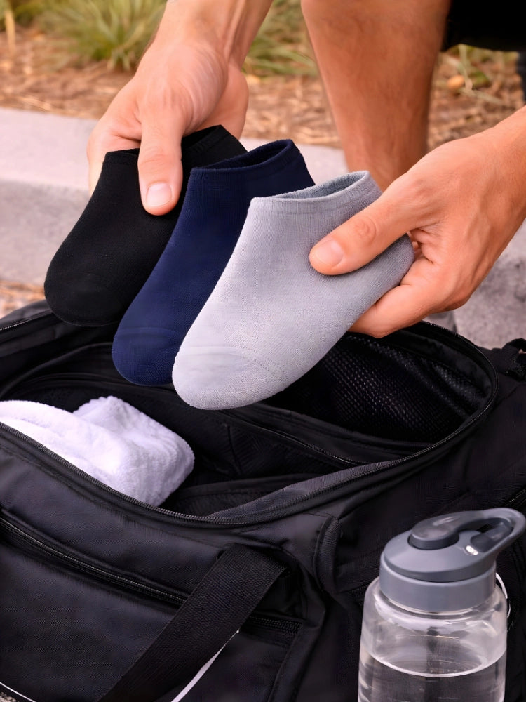 Person holding black, blue, and gray socks with a water bottle in the foreground.