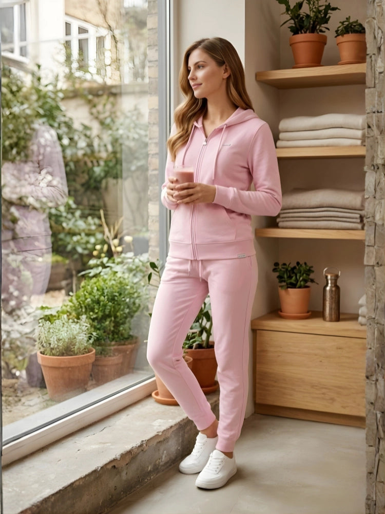 Woman in pink tracksuit standing by a window holding a cup, with plants and shelves in the background.

Ladies' baby pink zip-up hoodie and jogger tracksuit set by Stylewar
