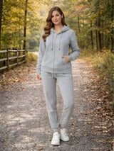 Woman in a gray tracksuit standing on a path in a forest during autumn.