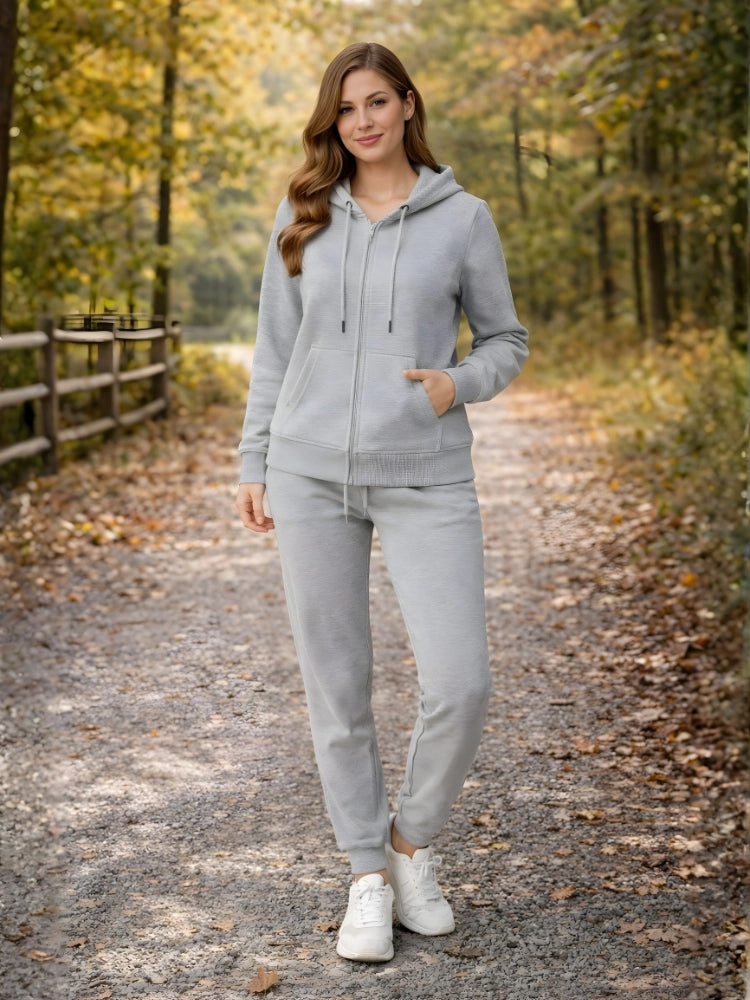 Woman in a gray tracksuit standing on a path in a forest during autumn.
