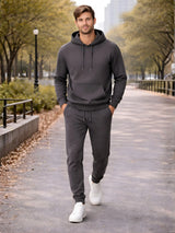 Man wearing a gray hoodie and jogger pants walking on a path with trees and buildings in the background. 

Dark grey men’s pullover hoodie with matching jogger trousers by Stylewar