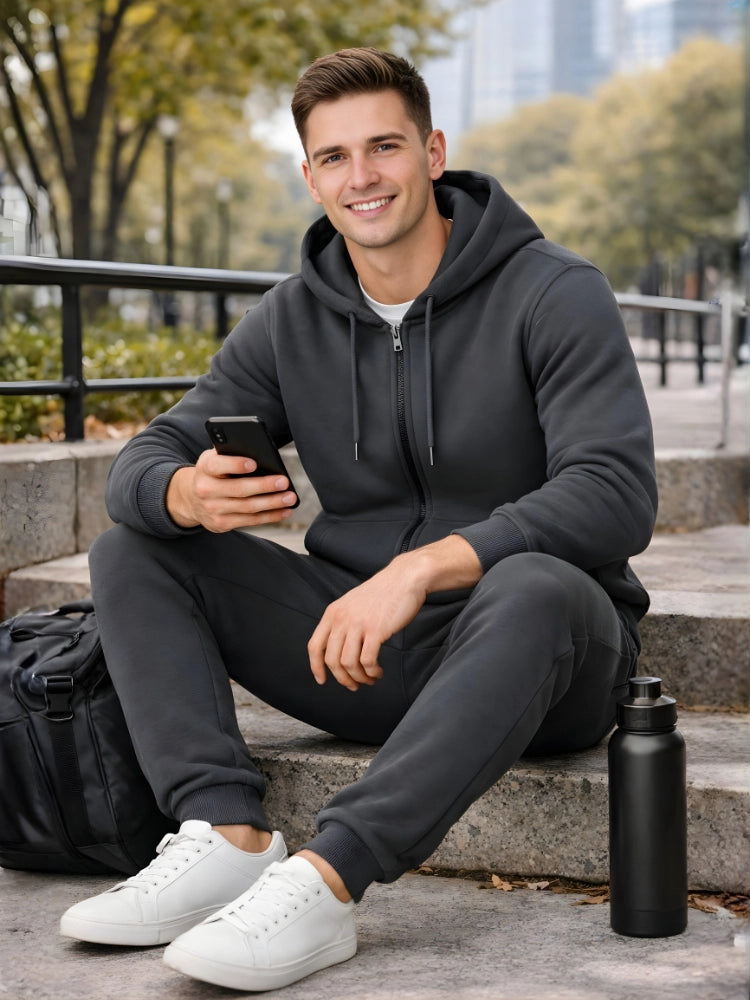 Man sitting outdoors holding a phone, wearing a dark hoodie and pants with white sneakers.

Dark grey men’s zip hoodie with matching jogger trousers by Stylewar