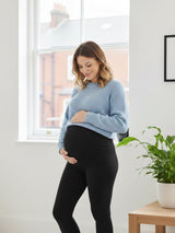 Pregnant woman wearing a light blue sweater and black leggings indoors.